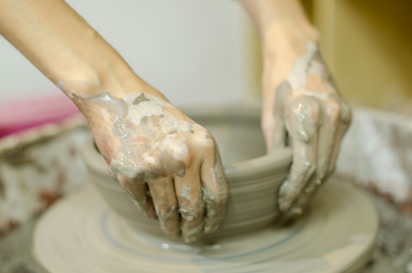 Hands covered in wet clay shaping pottery on a wheel.