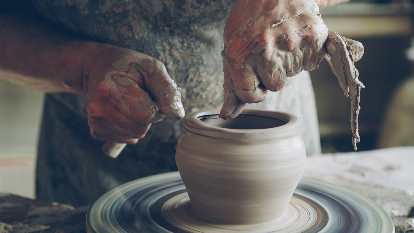 Hands shape a wet clay pot on a spinning wheel.